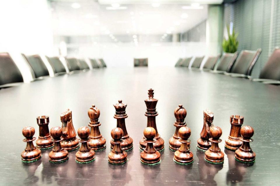 Chess pieces set for play down a boardroom table, the chairs and the head seat in view, representing strategy at the executive level